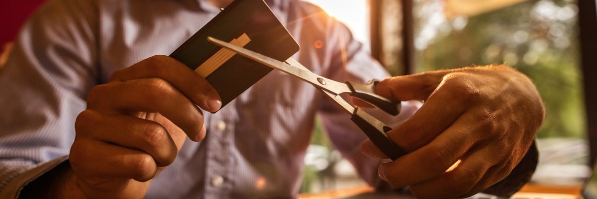 Man with massive beard cutting up credit card with pair of scissors.