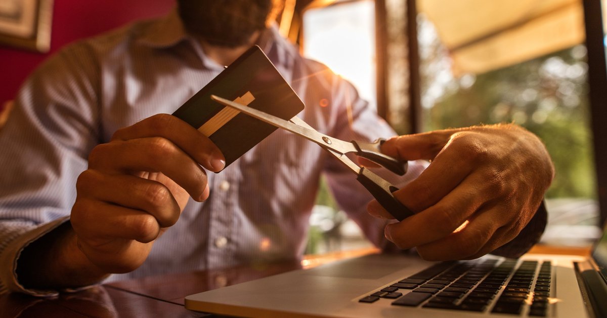Man with massive beard cutting up credit card with pair of scissors.