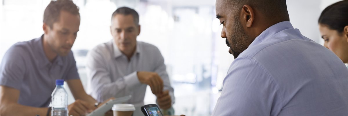 Man appearing frustrated looking at his cell phone while seated among group of people