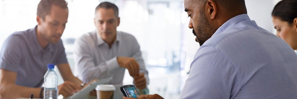 Man appearing frustrated looking at his cell phone while seated among group of people