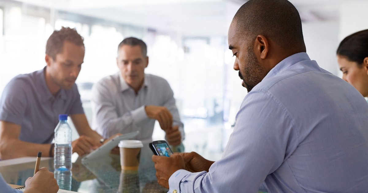 Man appearing frustrated looking at his cell phone while seated among group of people