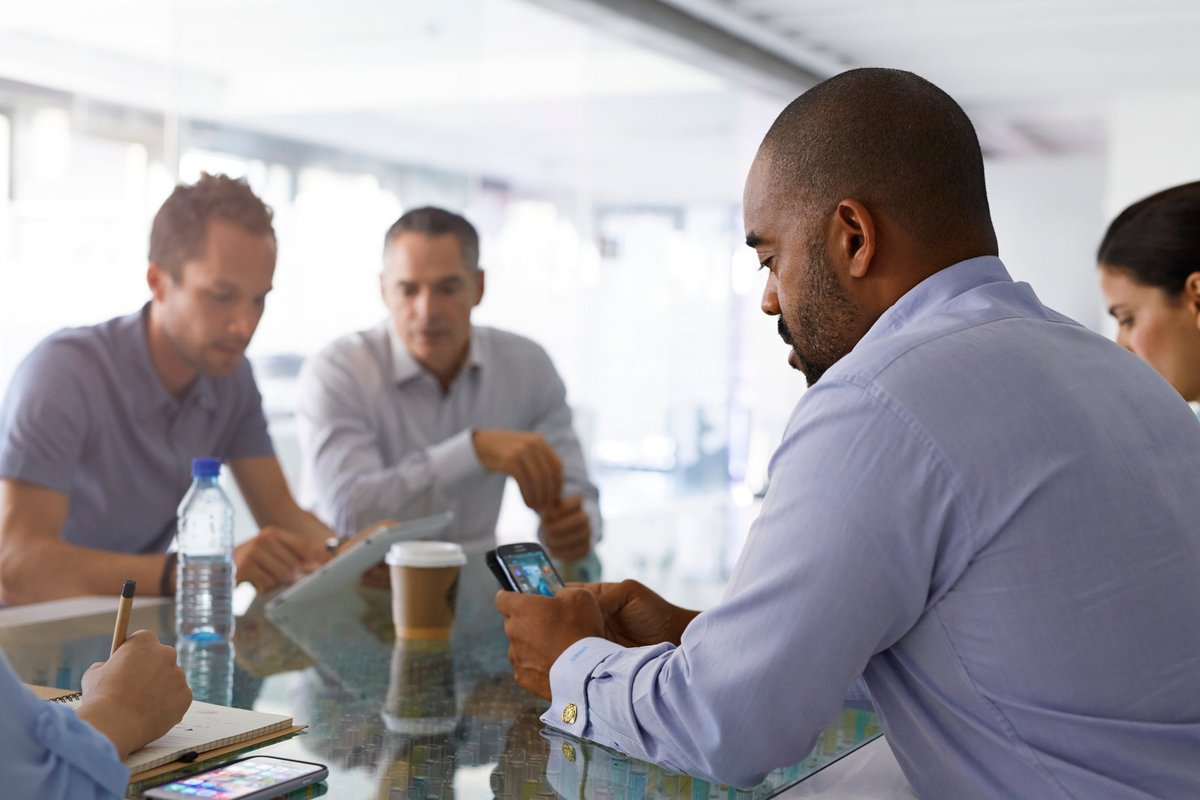 Man appearing frustrated looking at his cell phone while seated among group of people