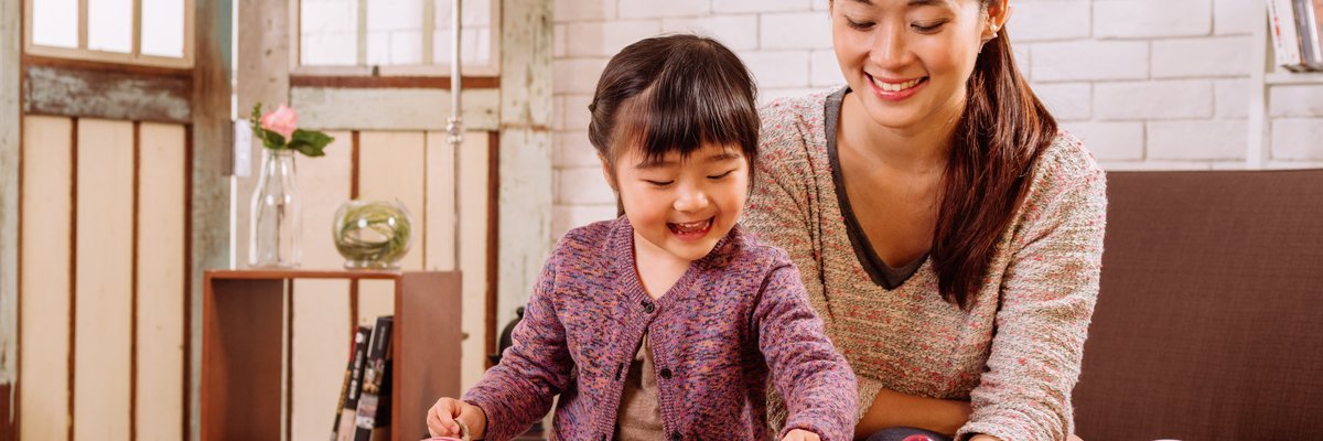 A child puts coins into differently sized piggy banks under the happy supervision of her parent.