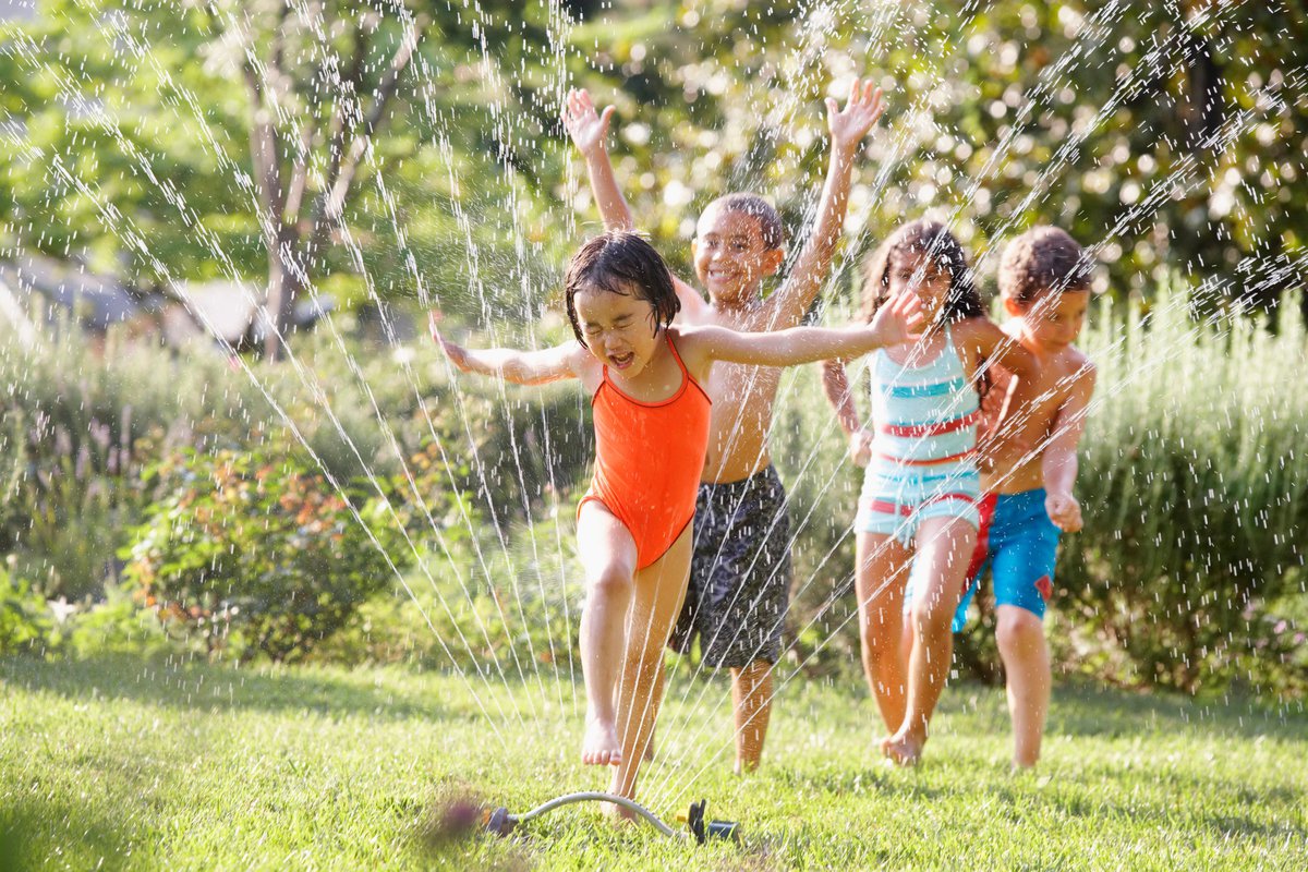 Children wearing bathing suits run through a sprinkler joyfully.