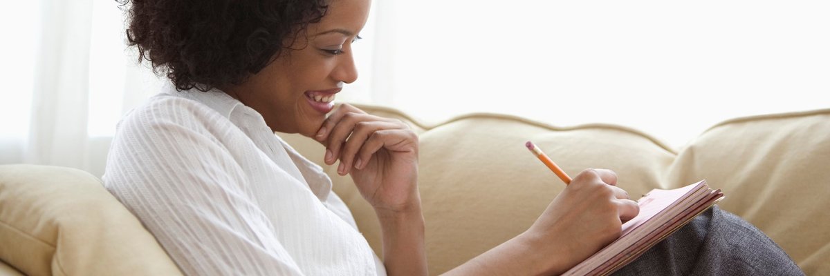 A person reclines on their couch while writing with a notepad.