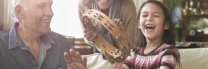 Grandparents and grandchild play bongos and tambourine together in their home.