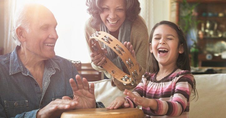 Grandparents and grandchild play bongos and tambourine together in their home.