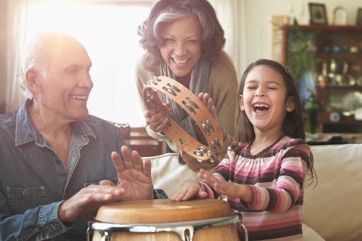 Grandparents and grandchild play bongos and tambourine together in their home.