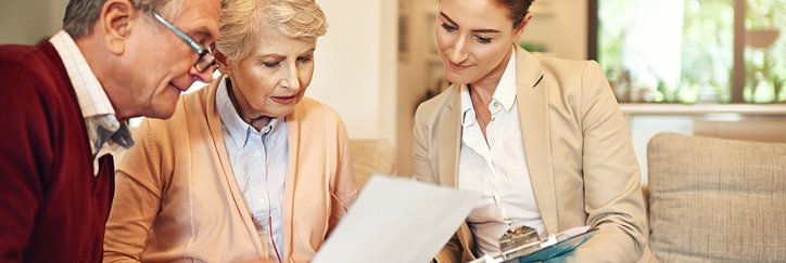 A mature couple discusses paperwork with a businesswoman in a home.