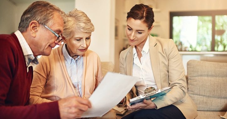 A mature couple discusses paperwork with a businesswoman in a home.