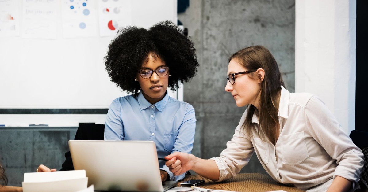 Two business workers discuss pie charts and financial papers while one of them points at a computer screen.