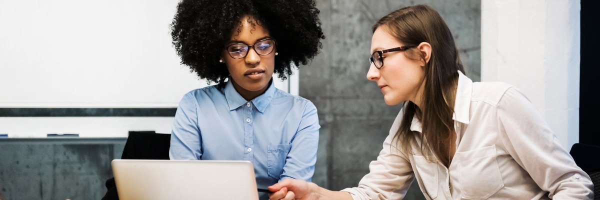 Two business workers discuss pie charts and financial papers while one of them points at a computer screen.