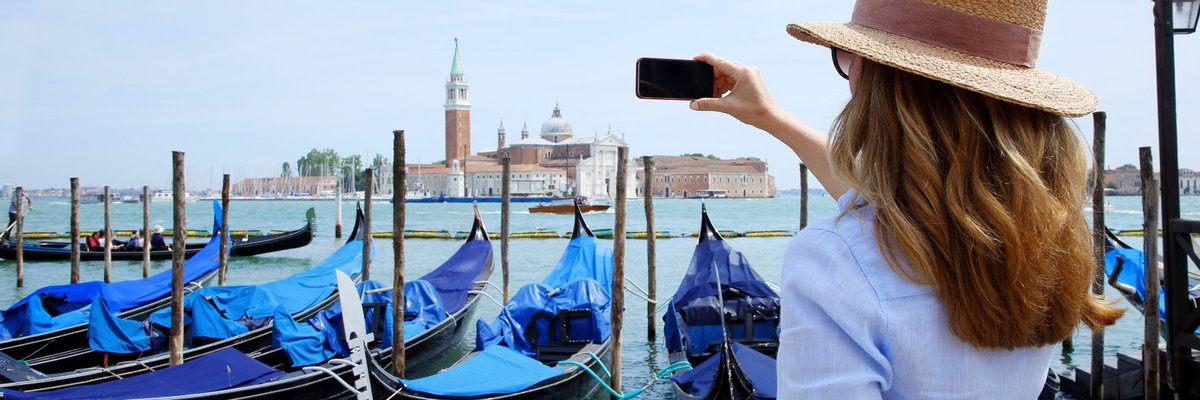 Woman in hat facing away and taking photos of an enormous old church across a bay.