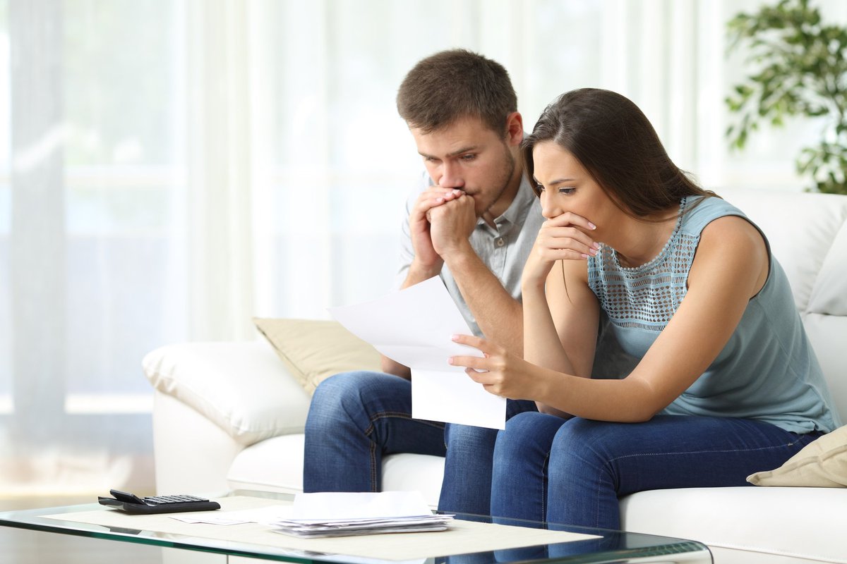 concerned man and woman sitting on couch looking at paperwork