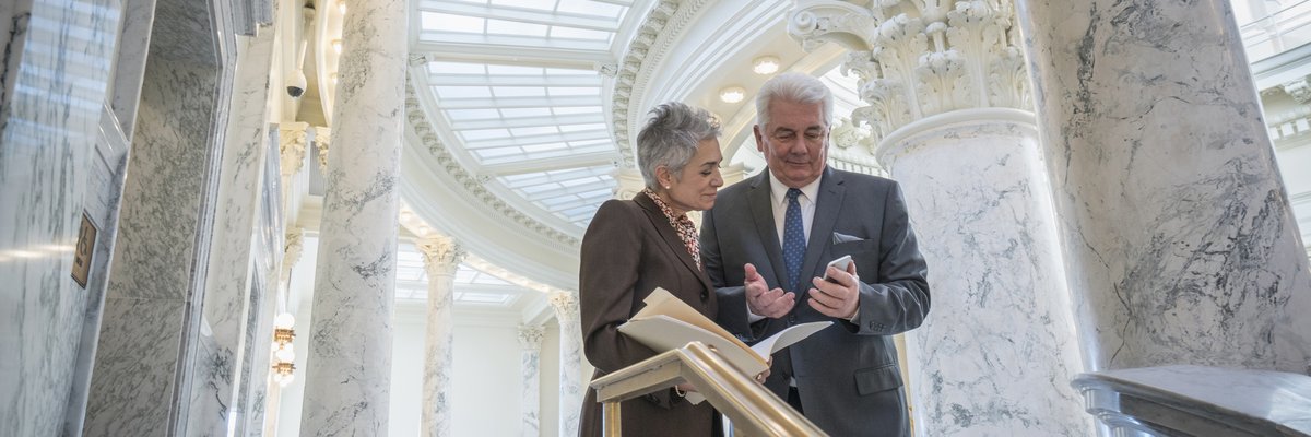 Two mature businesspeople discuss financial matters in a federal building.