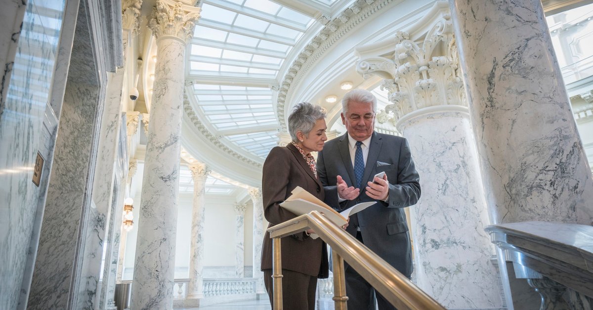 Two mature businesspeople discuss financial matters in a federal building.