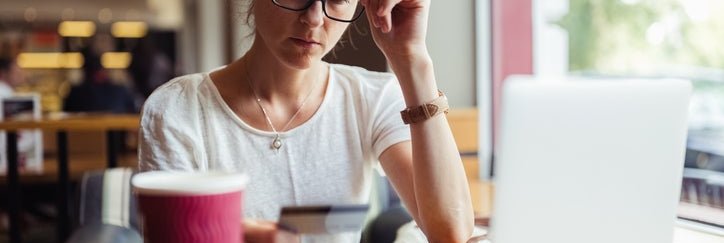 A woman looks at her credit card in confusion while sitting in a café.