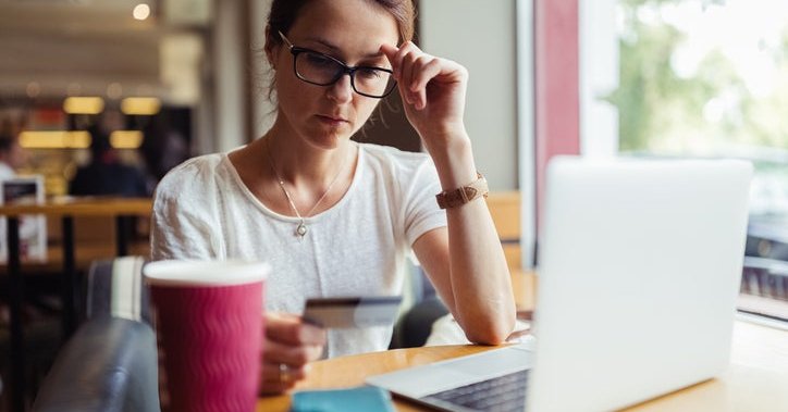A woman looks at her credit card in confusion while sitting in a café.