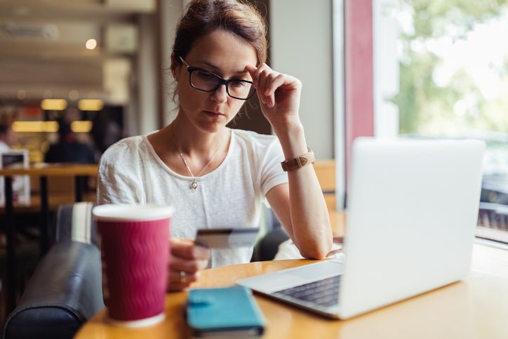 A woman looks at her credit card in confusion while sitting in a café.