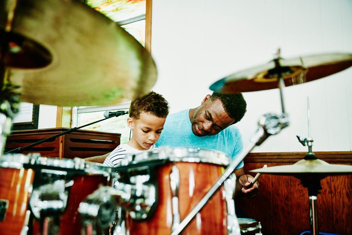 Father sits with young son at a drum set.