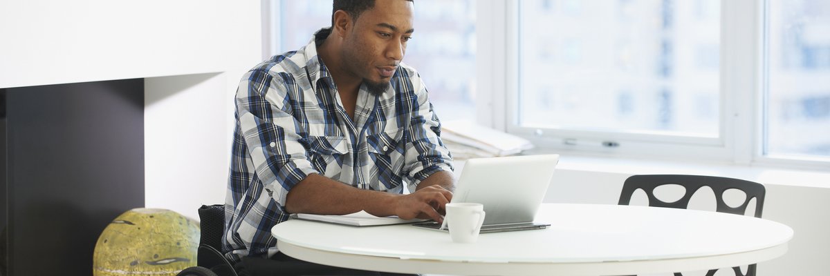 A person using a wheelchair types on a tablet while sitting at a table in a public space.