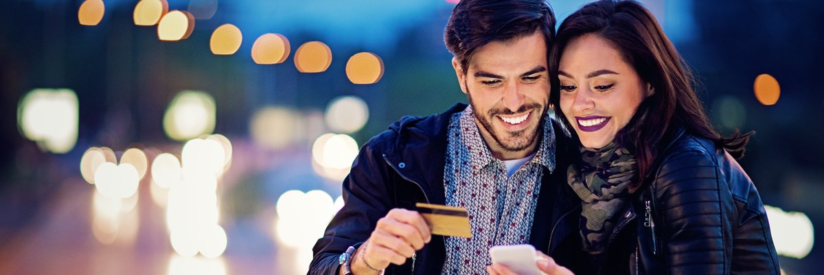 Couple smile while holding credit card and looking at cellphone.