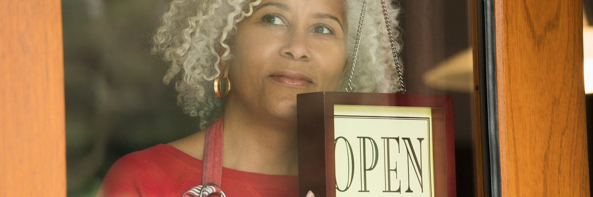 A person holds the "Open" sign on the front door of a small business.