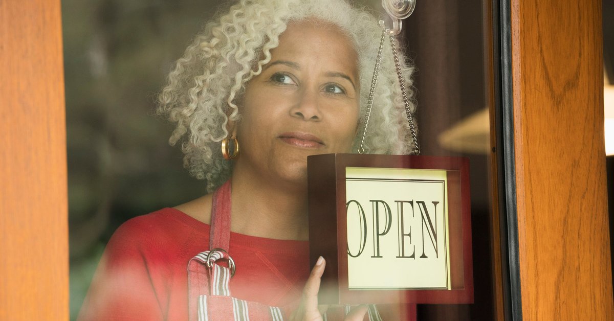 A person holds the "Open" sign on the front door of a small business.