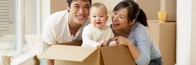 A couple smiles at a baby as they unpack moving boxes in their new home.
