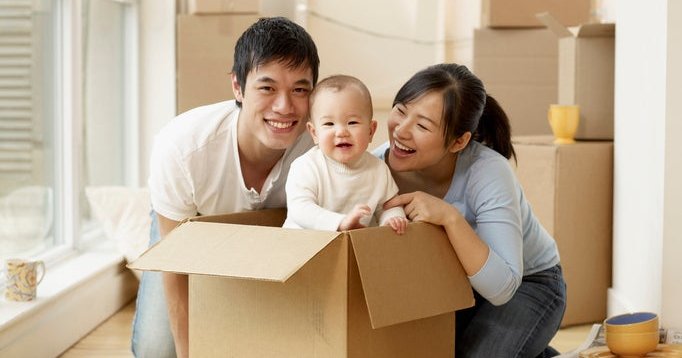 A couple smiles at a baby as they unpack moving boxes in their new home.