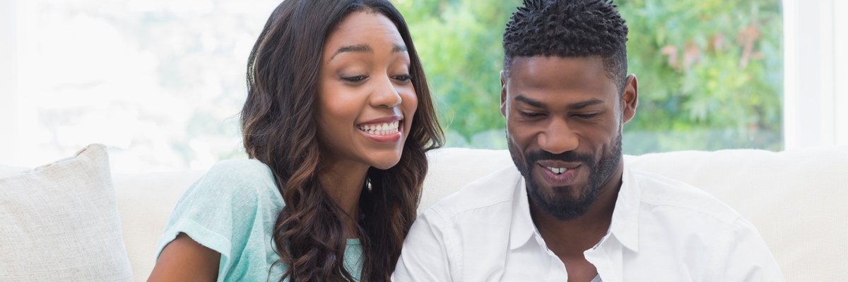 young man using laptop and young woman holding credit card sitting next to each other on a couch.