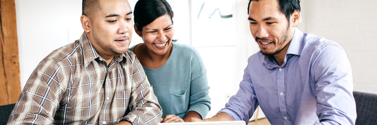 Three people smile as they look at paperwork in an office.