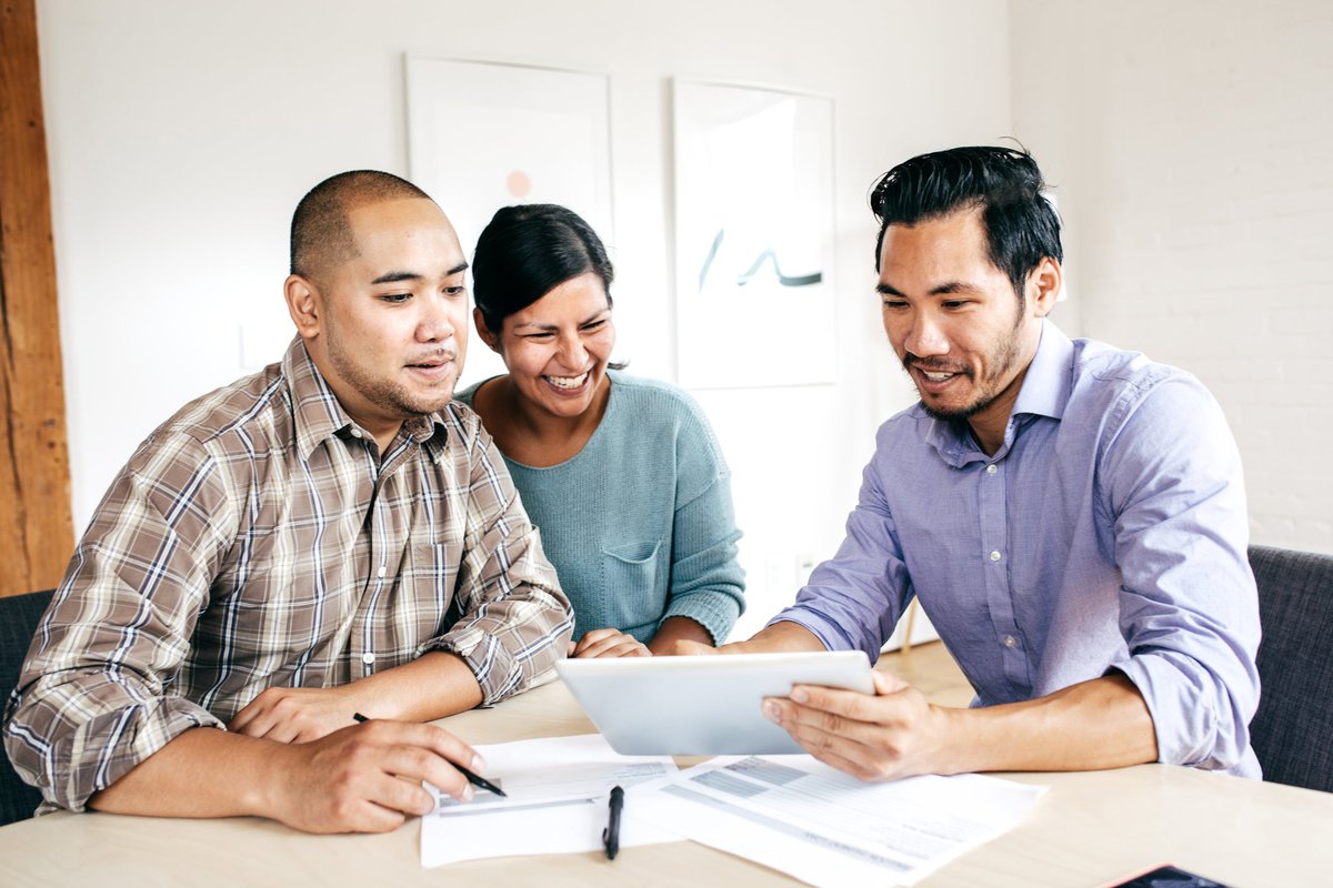 Three people smile as they look at paperwork in an office.