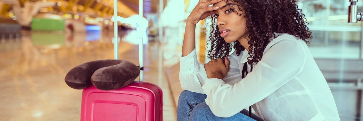 Woman sitting beside luggage at airport looking stressed.