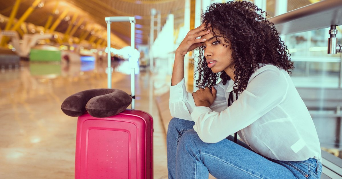 Woman sitting beside luggage at airport looking stressed.