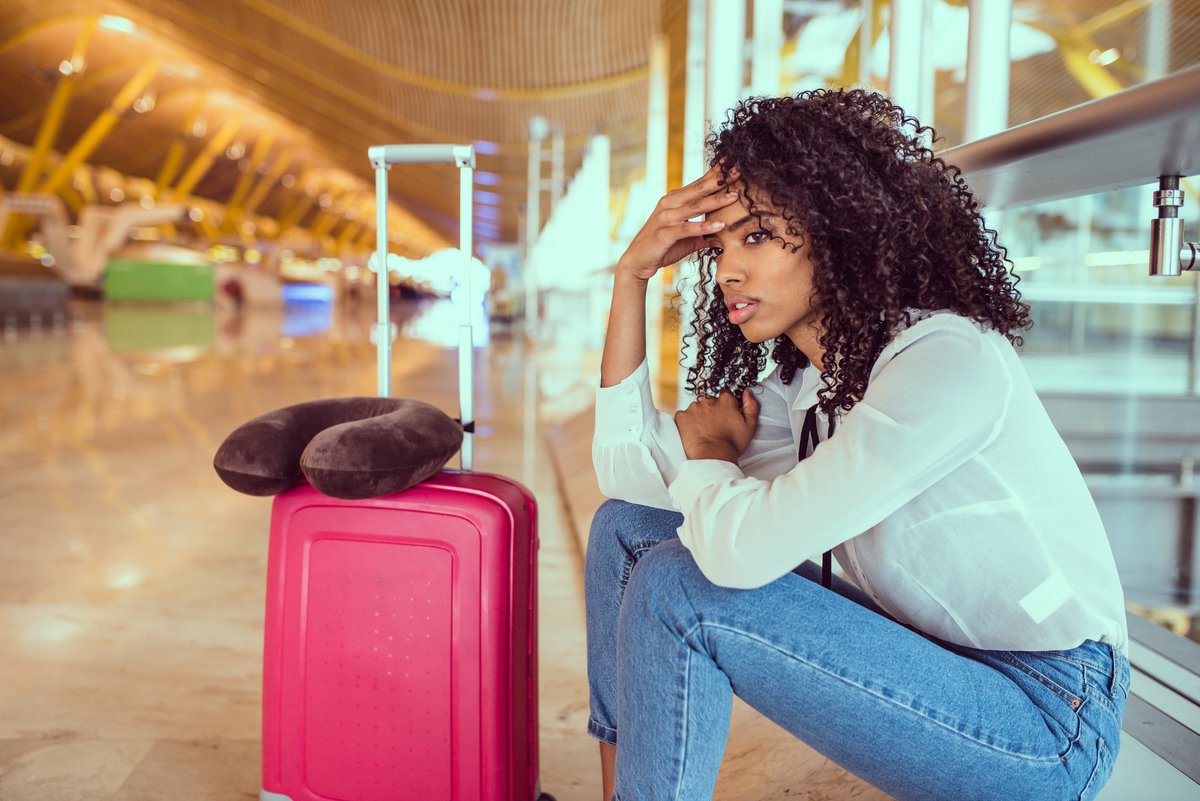 Woman sitting beside luggage at airport looking stressed.