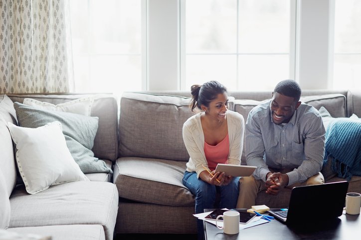 A happy couple looks at paperwork and a laptop in their living room