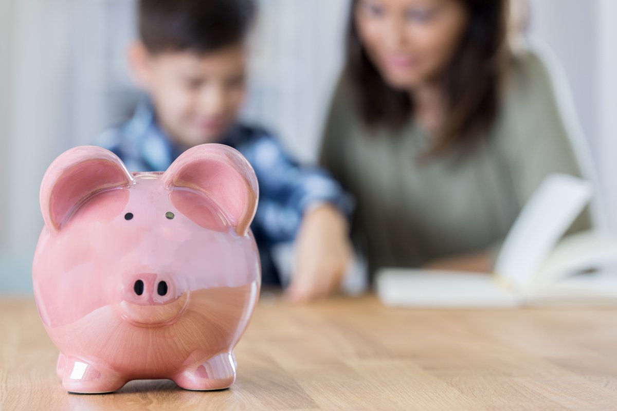 A piggy bank with a mother reading to her son in the background.