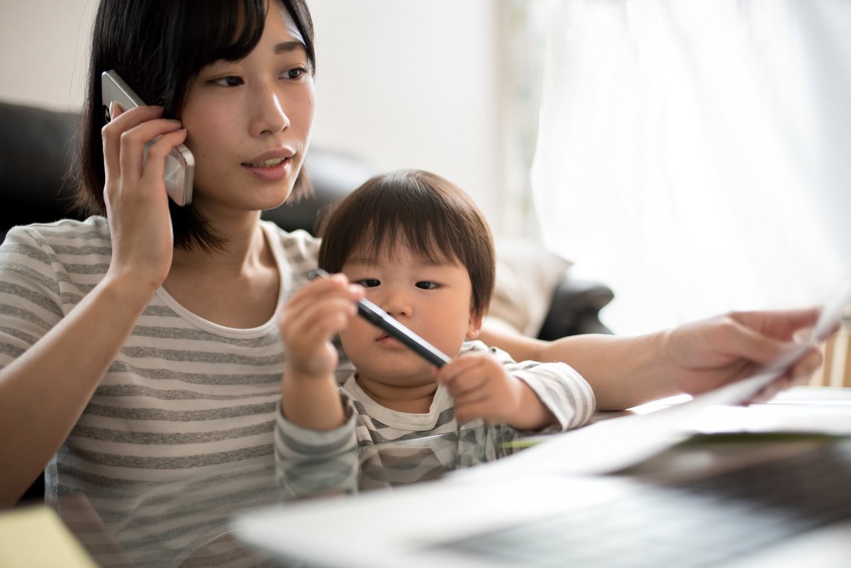 woman talking on phone while toddler sits on her lap playing with a pen.