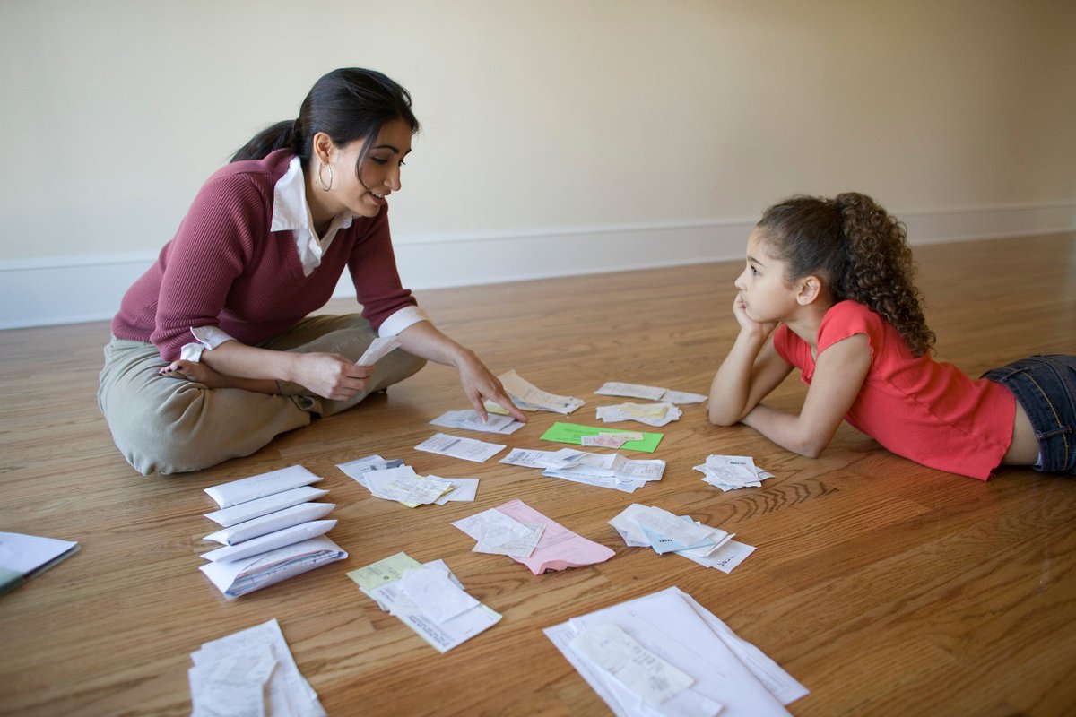 Ein Elternteil und ein Kind sortieren Rechnungen, die auf dem Boden sitzen.