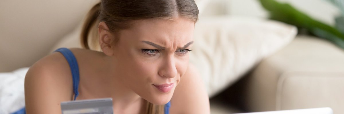 Young woman holding credit card and looking at laptop screen suspiciously.