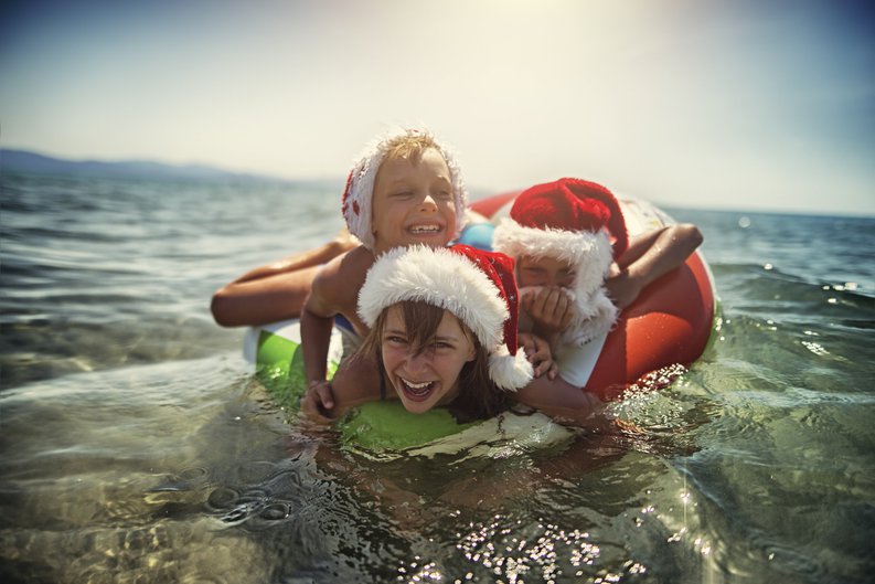 A woman and two children, all wearing Santa hats, swimming in the ocean together.