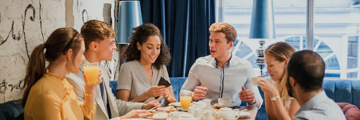 Group of young adults sitting around a table conversing and sharing a meal.
