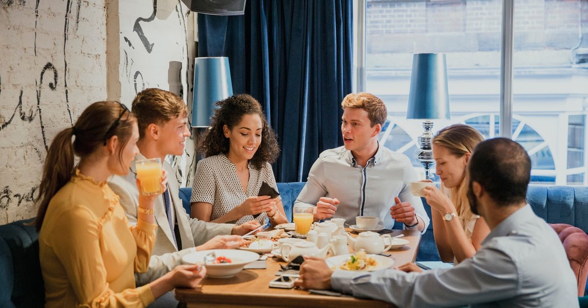 Group of young adults sitting around a table conversing and sharing a meal.