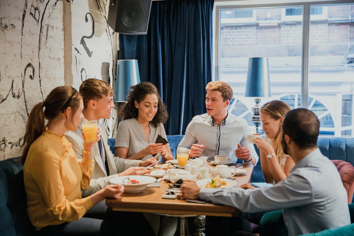 Group of young adults sitting around a table conversing and sharing a meal.