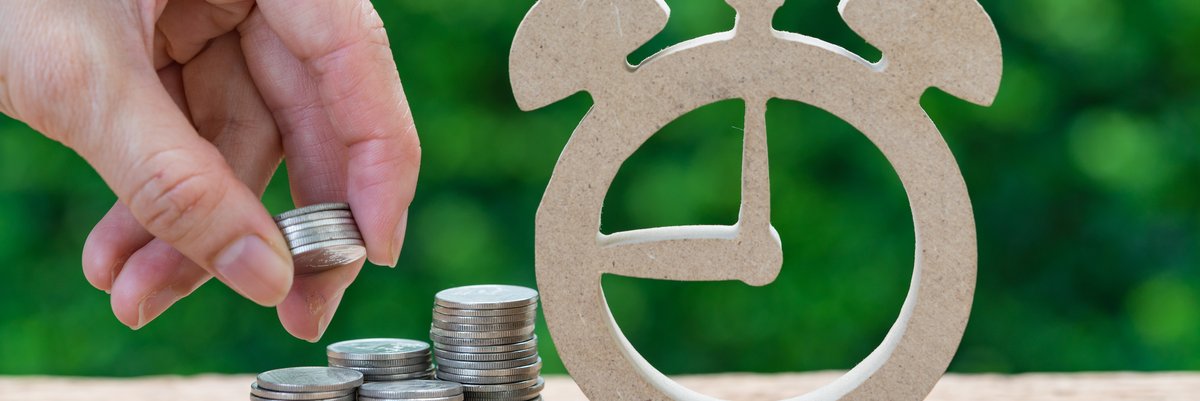 A hand makes stacks of coins next to a cardboard cutout of an alarm clock.