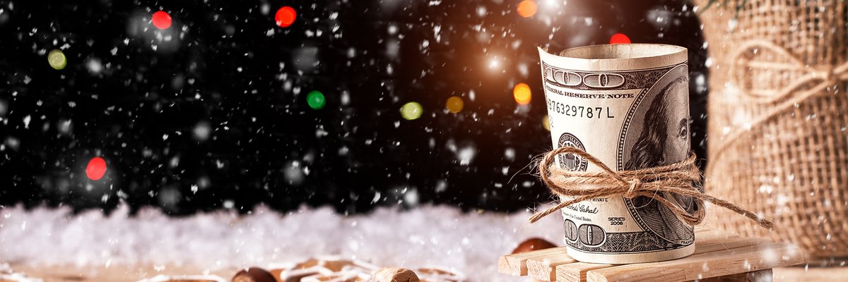 A 100-dollar bill tied with a thin rope amid snow, pine cones, and Christmas ornaments.