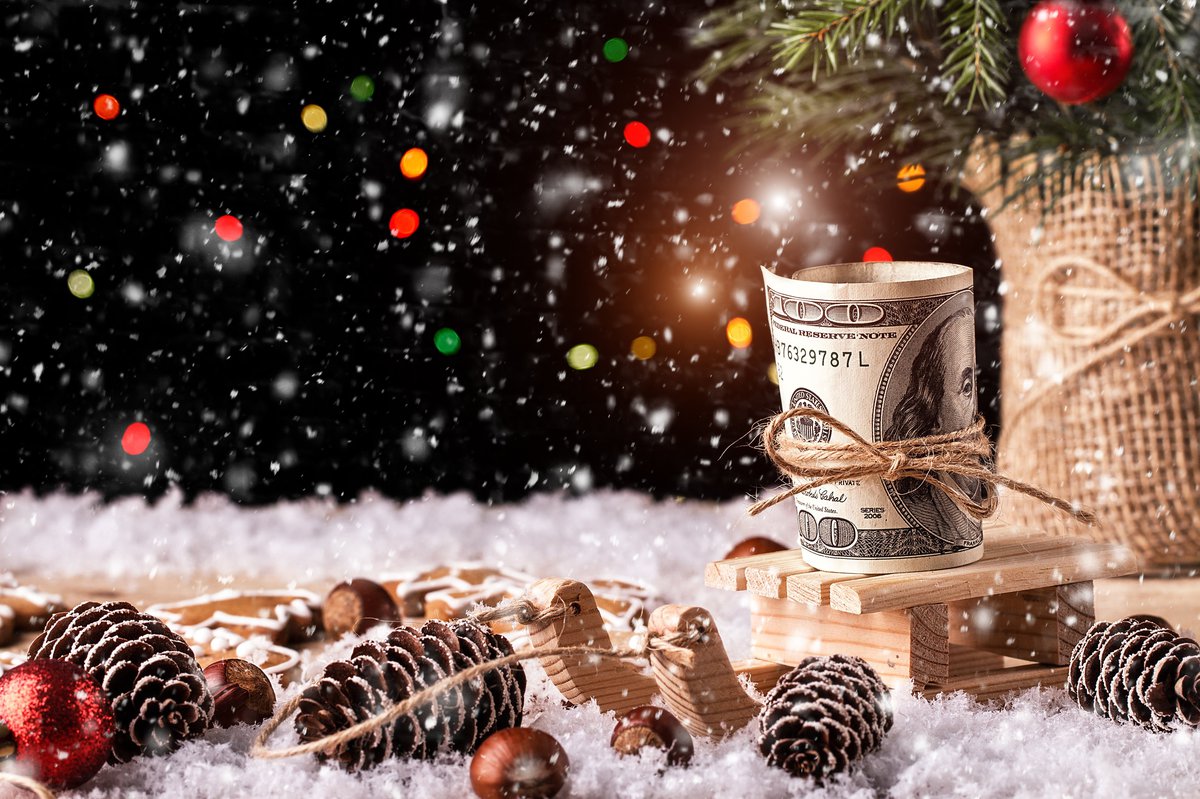 A 100-dollar bill tied with a thin rope amid snow, pine cones, and Christmas ornaments.