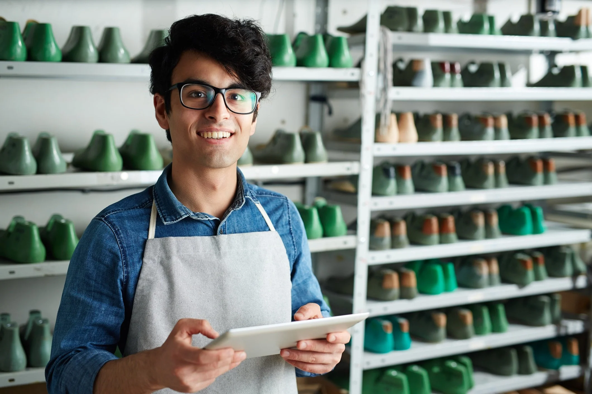 A shoemaker in an apron with a laptop.