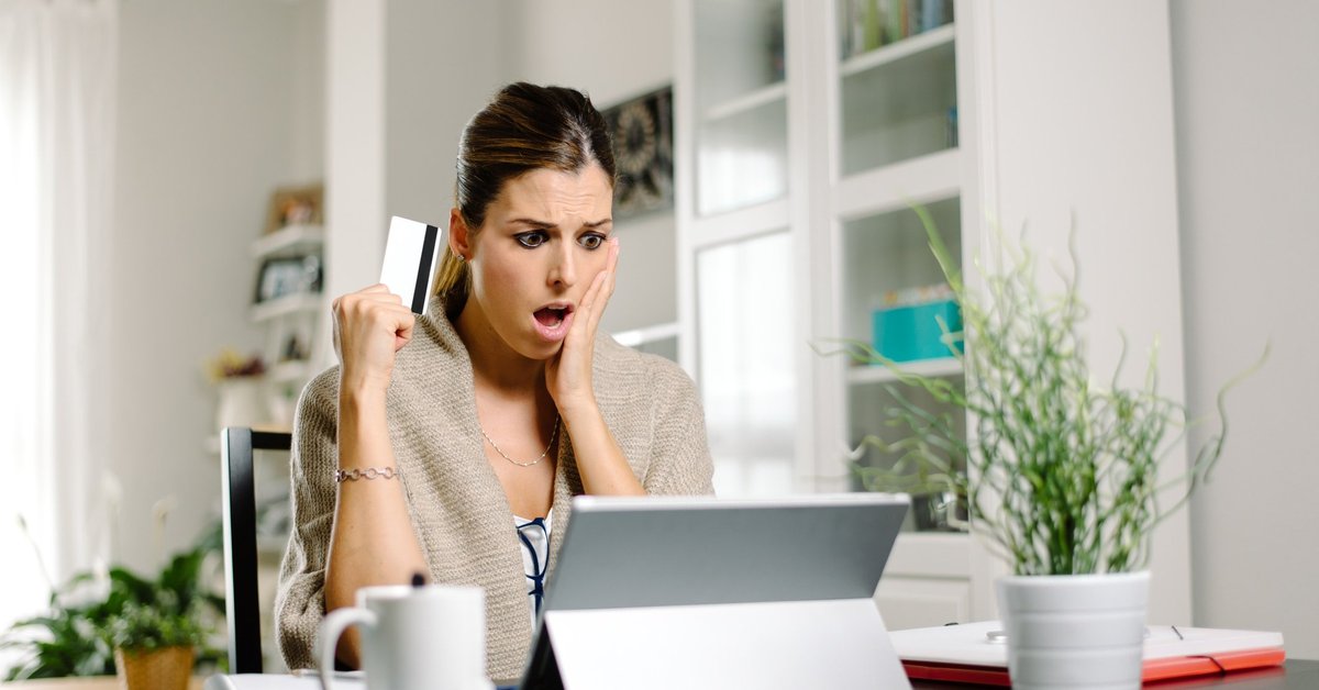 Shocked woman with credit card in hand looking at credit card score on iPad